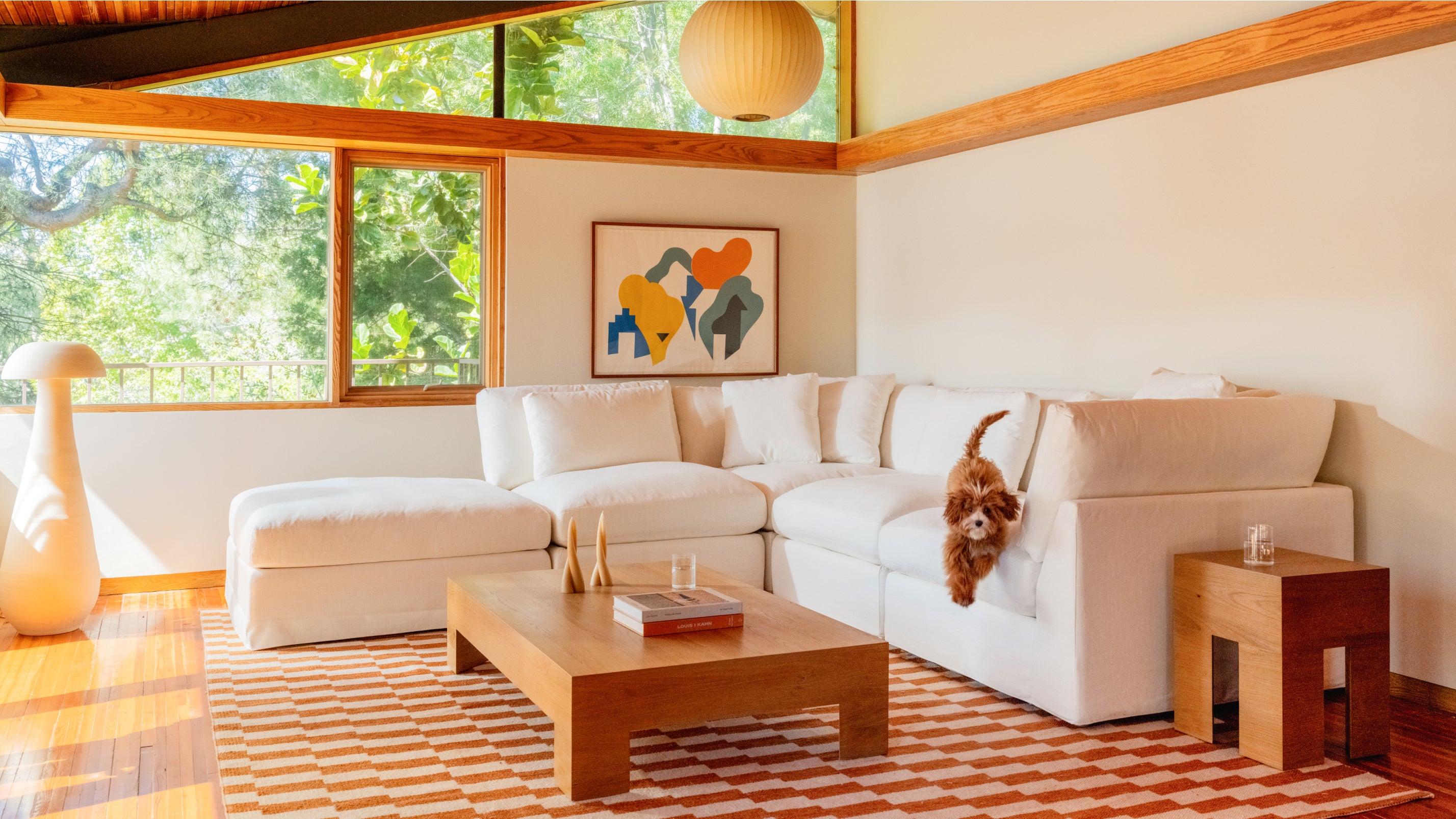 Modern living room with a white sectional sofa, wooden coffee table, and colorful abstract art on the wall.